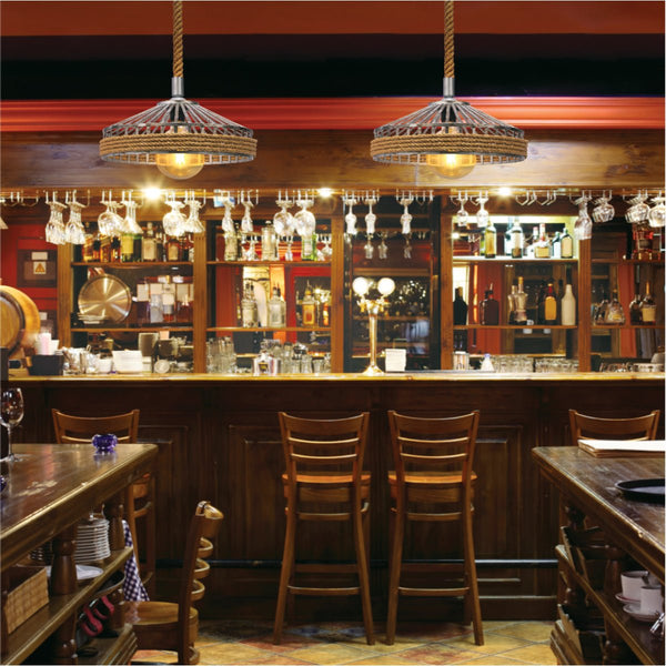 Rustic bar scene: wooden bar, stools, shelves stocked with glassware and liquor. Pendant lights add a warm glow.