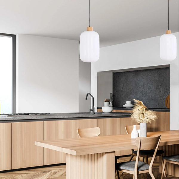 Two stylish pendant lights hang above a wooden dining table in a modern kitchen, adding a touch of elegance to the space.