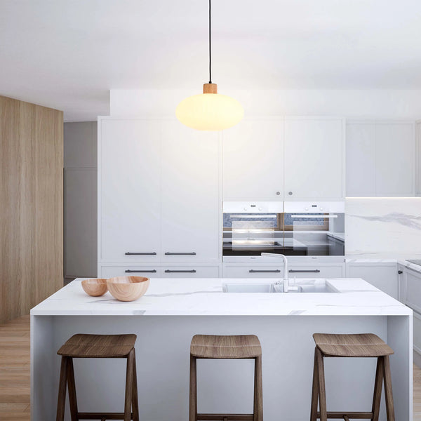 A minimalist kitchen with a pendant light, featuring a round, frosted glass shade and a wooden accent, suspended above a marble island.